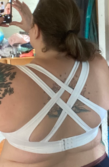 A reviewer displays the back view of a white sports bra with four crisscrossed straps.