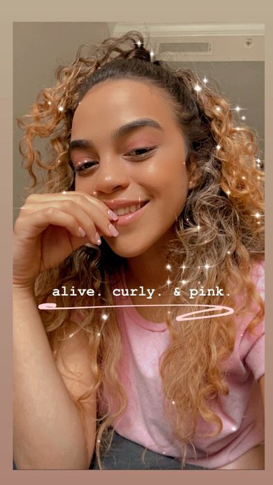 A reviewer with curly hair smiles, resting her hand on her chin. The image features the text, 