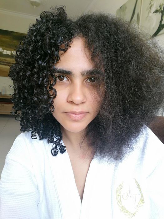 The reviewer demonstrates one side of their hair styled with a curling brush, while the other side is air-dried without the use of a brush.