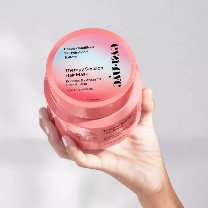A hand holding a jar of Eva NYC Therapy Session Hair Mask, with the label highlighting benefits such as deep conditioning, triple hydration, and ingredients like argan oil and plant protein