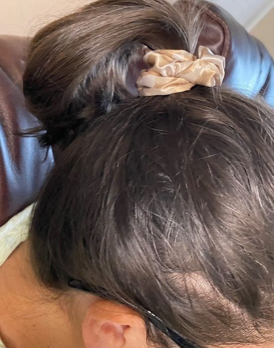 A person with glasses sits on a leather chair, their hair styled in a bun secured by a scrunchie, viewed from above.