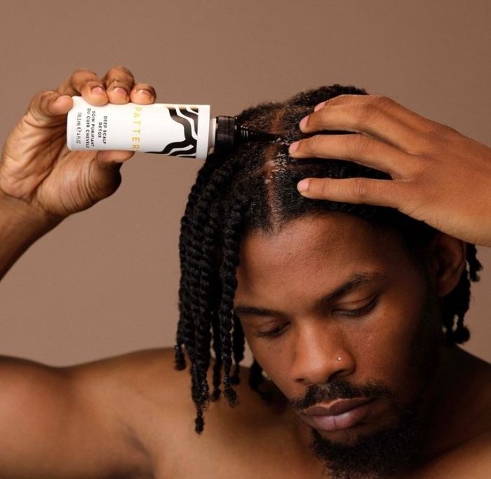 A person applying matte hair oil to their scalp, with a bottle in hand, demonstrating a hair care routine