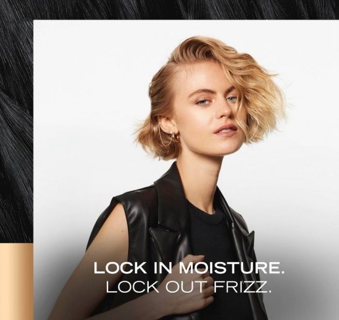 A model with a chic short haircut, dressed in a sleeveless leather jacket, featured in a beauty advertisement with the tagline: "Lock in moisture. Lock out frizz."