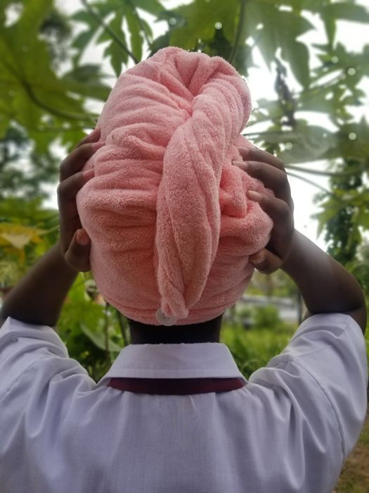 A reviewer, facing away from the camera and wearing a white shirt, holds a large pink towel wrapped around their head
