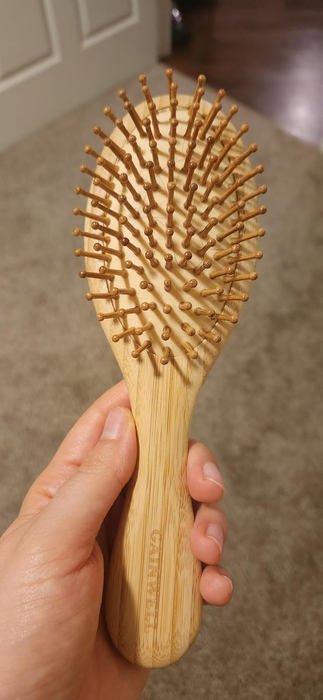 A wooden hairbrush with rounded bristles held in hand, ideal for gentle detangling and soothing scalp massages.