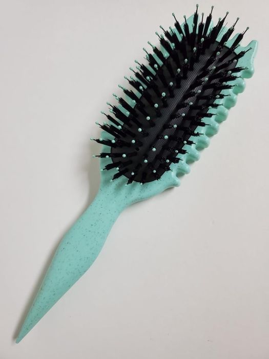 A hairbrush featuring a textured, ergonomic handle and tightly packed bristles, displayed against a neutral backdrop