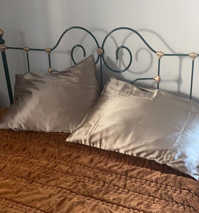 A reviewer’s photo of a neatly made bed featuring a cast-iron headboard, two silk pillows, and a brown textured bedspread