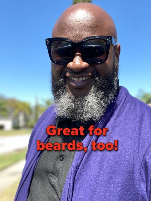 A bearded person wearing sunglasses and a shawl smiles at the camera. Text overlay reads, 
