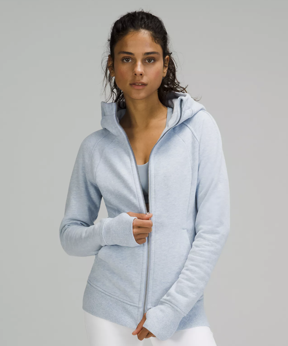 A model is seen wearing a pale blue zippered hoodie with thumbholes.