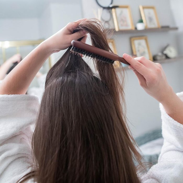 The model is adding volume to their hair with a teasing brush.