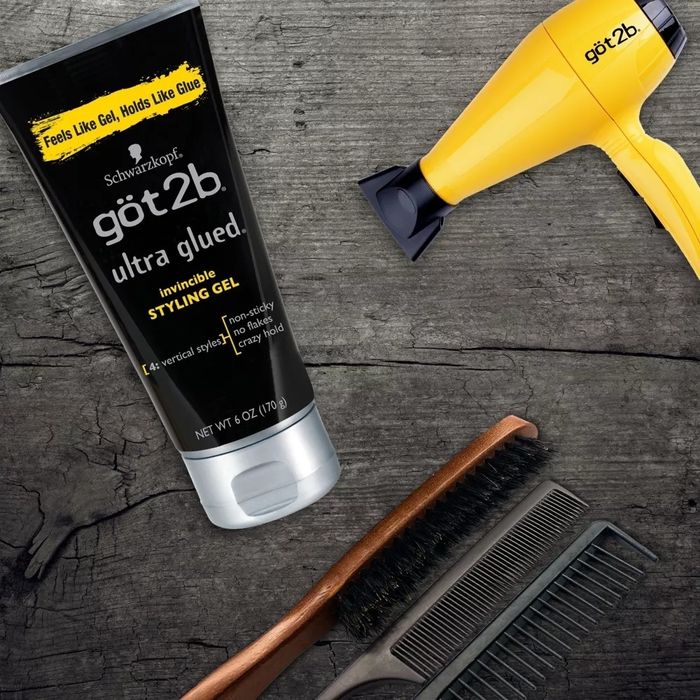 Got2b styling gel, a yellow hairdryer, a brush, and a comb arranged on a wooden surface, showcasing essential hair styling tools