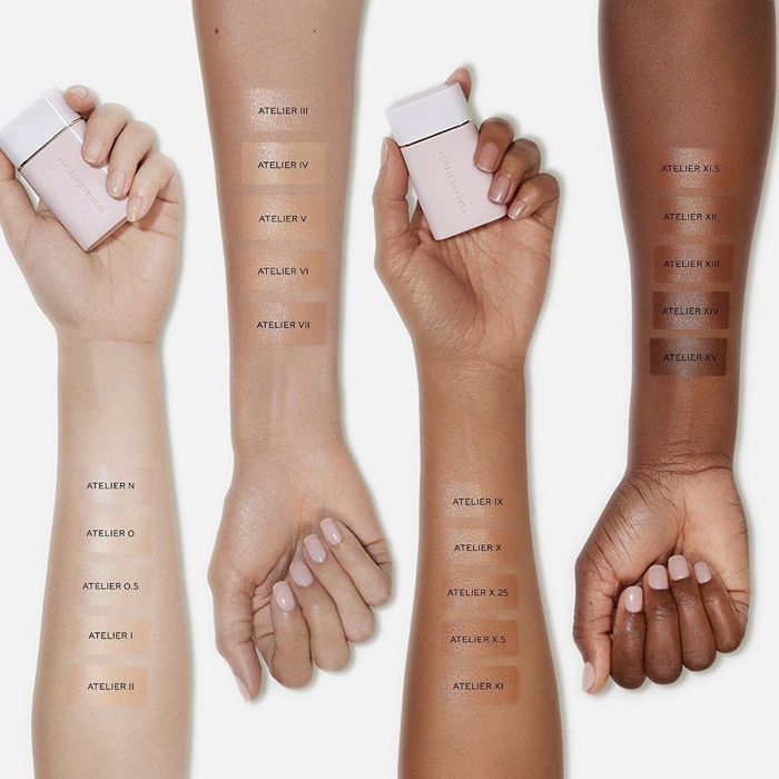 Four hands with varying skin tones holding cosmetic bottles, displaying nine foundation shades labeled Atelier II to Atelier X.5 on their arms
