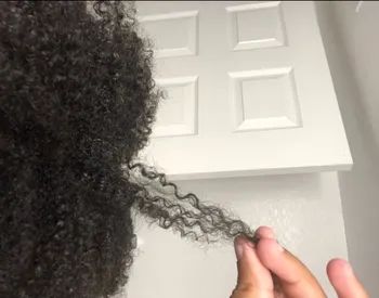 Reviewer with curly hair holding out a strand of their hair
