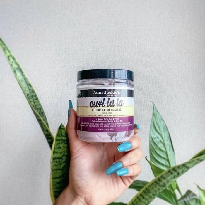 A jar of curl custard held by someone, with lush green leaves in the backdrop