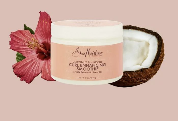 A jar of curl smoothie alongside a sliced coconut and a pink flower