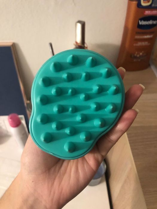a reviewer holding the green scalp massager in their hand
