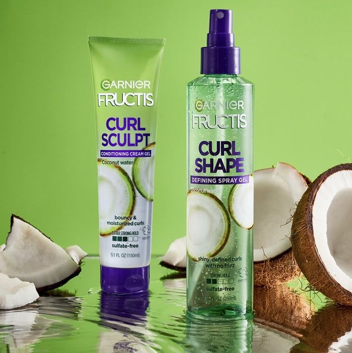 A bottle of cream-gel and defining spray gel alongside sliced coconuts
