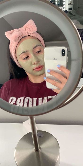 A reviewer wearing the pink headband while applying a clay face mask