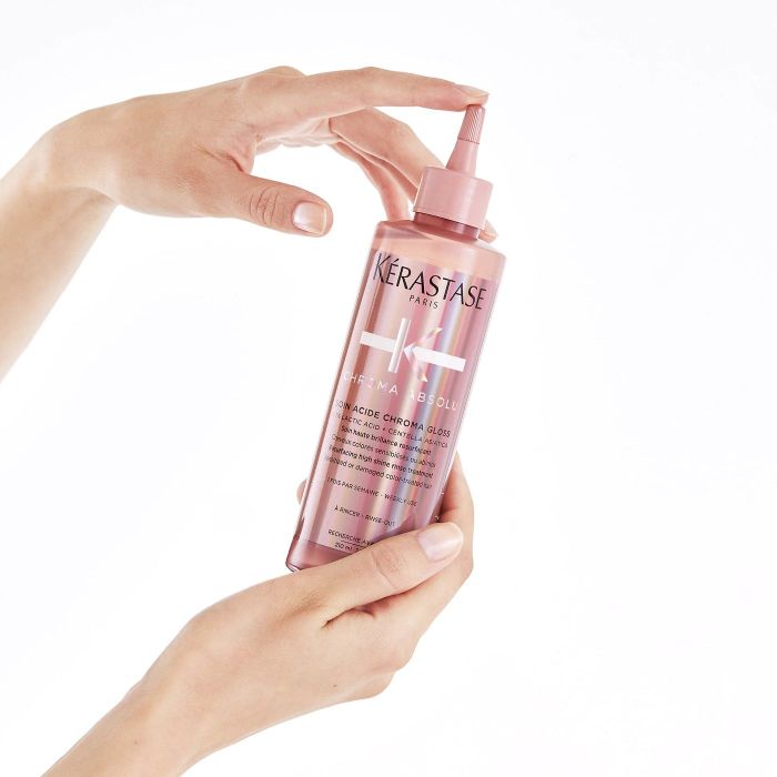 A pair of hands holding a pink bottle of hair gloss