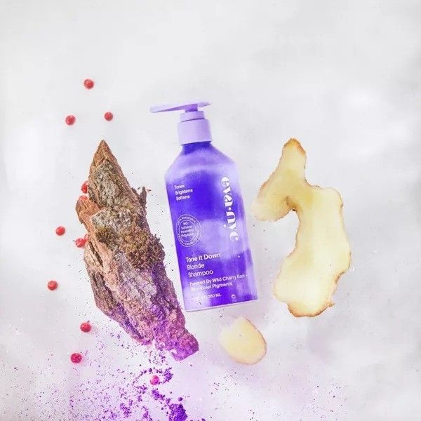 A purple shampoo bottle surrounded by bark, ginger, and pink peppercorns, hinting at its natural ingredients