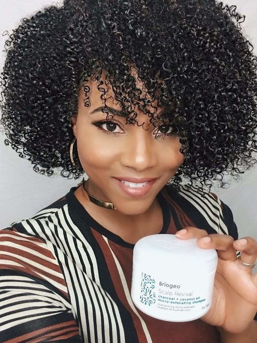 Model with stunning natural hair holding a container of the shampoo