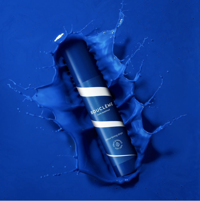 A blue and white striped bottle of hair toner submerged in a vibrant cobalt blue liquid