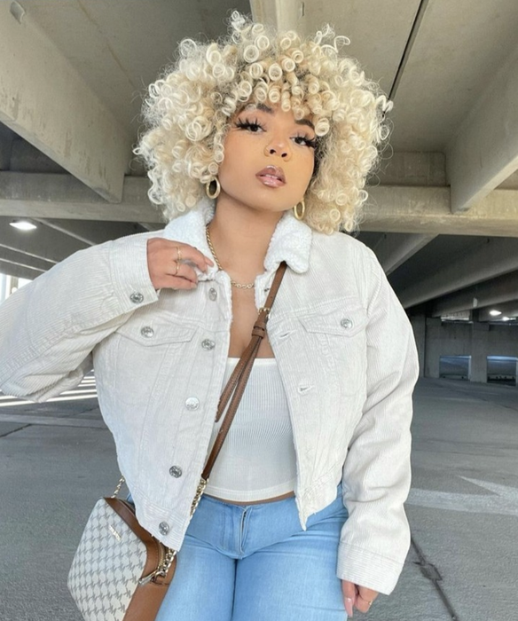 A model with light blonde curly hair posing in a parking garage