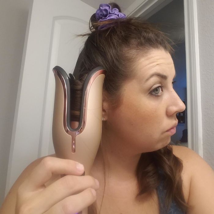 A reviewer using the curling iron to style their hair
