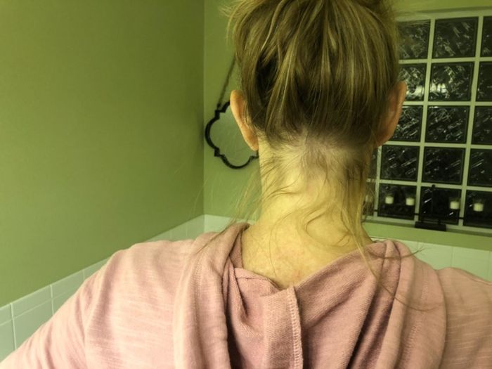 a before photo showing a reviewer with her hair in a bun, highlighting numerous loose flyaways and baby hairs around the edges