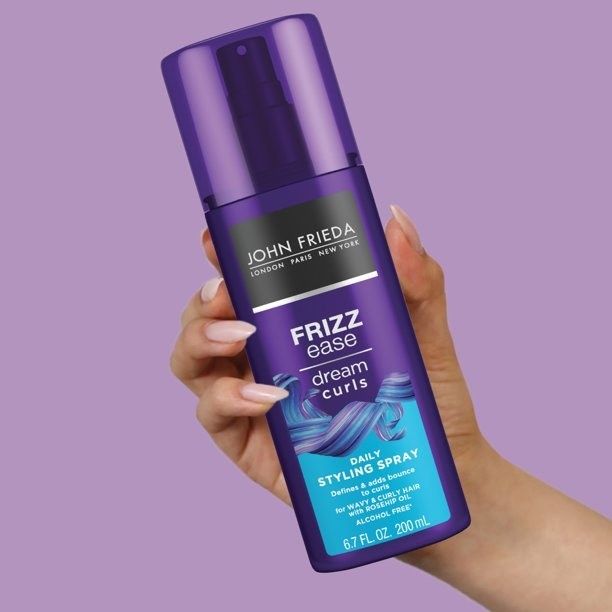 A person with pink nails holding a bottle of hairspray