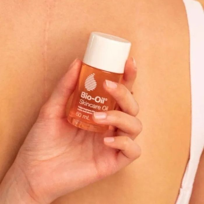 A person holding the bottle of oil discreetly behind their back