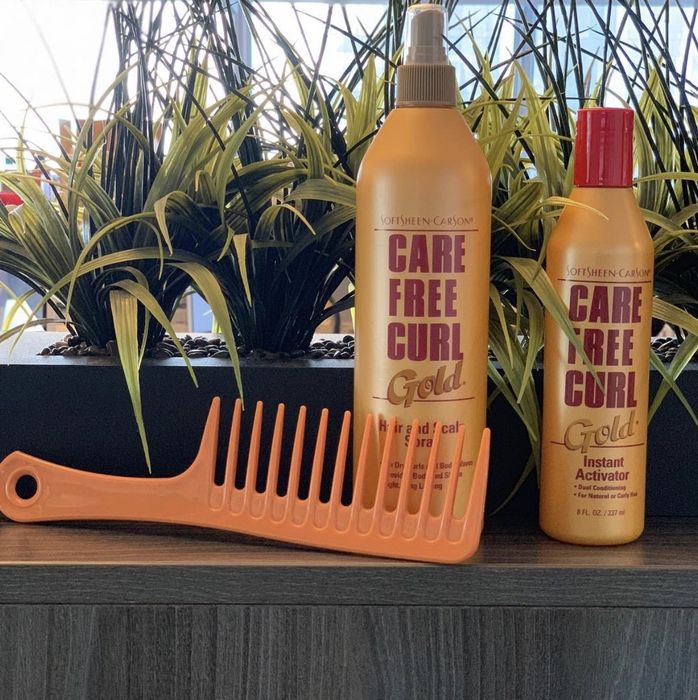 A bottle of curl activator and hair spray accompanied by an orange comb