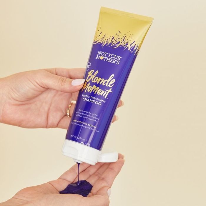 A person dispensing purple shampoo from a tube.