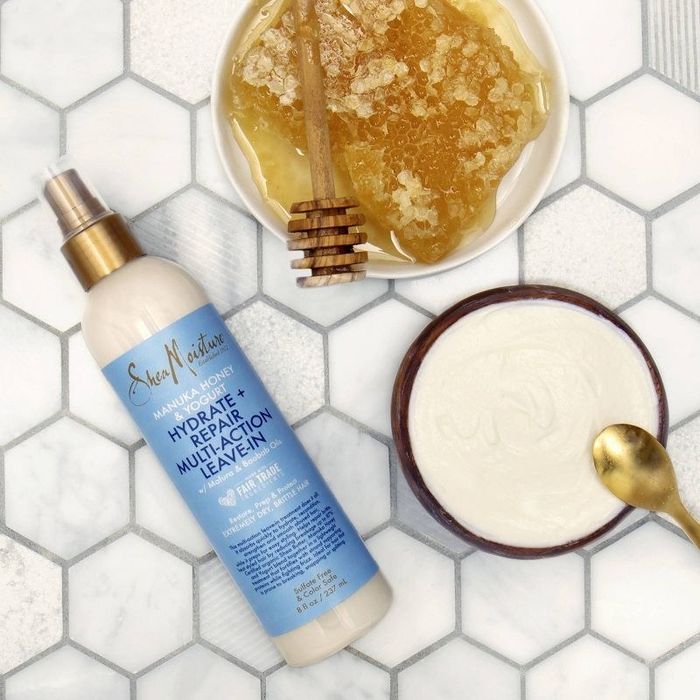 A bottle of leave-in conditioner next to a bowl of yogurt and honey.
