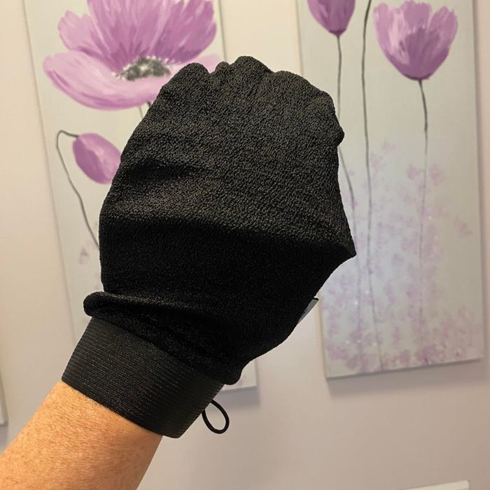 A reviewer modeling a sleek black exfoliating glove