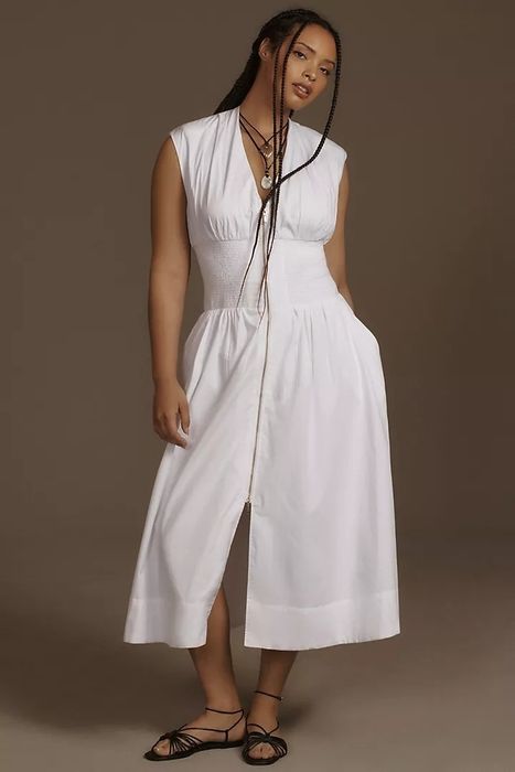 A model wearing a white pleated midi dress without sleeves, styled with strappy sandals