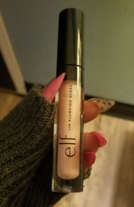 A reviewer holding a tube of light pink lip plumper.