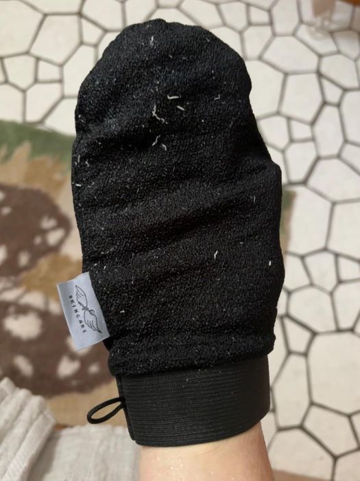 A detailed close-up of a reviewer’s hand adorned with a textured black exfoliating glove