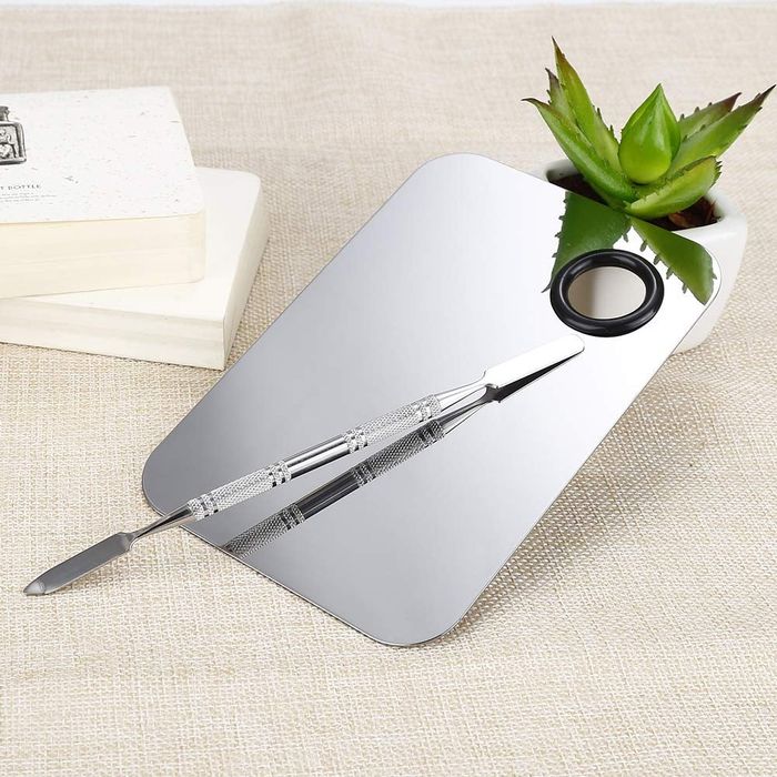 A stainless steel cosmetic palette and spatula elegantly placed next to a succulent plant.
