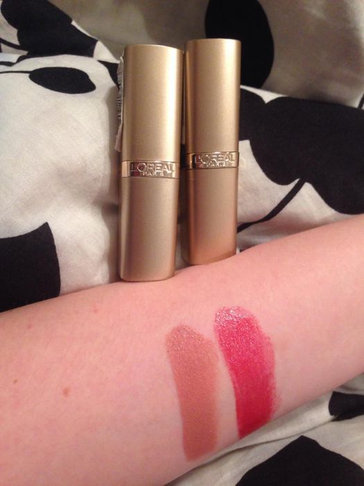a reviewer photo showing swatches of two lipstick shades on their arm, with the lipstick tubes visible in the background