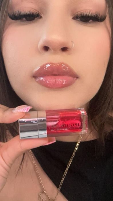 Reviewer holding a tube of lip gloss, showing off their glossy lips.
