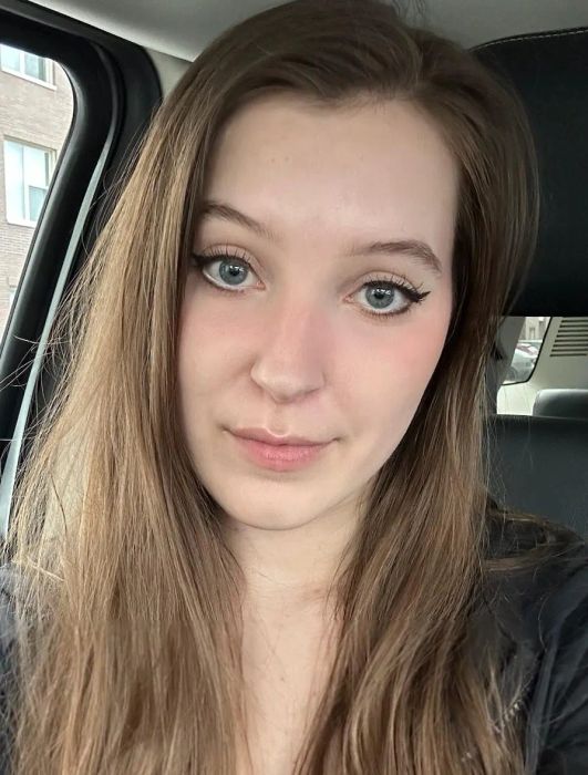 A reviewer sitting in a car, wearing a black top, smiling at the camera for a selfie