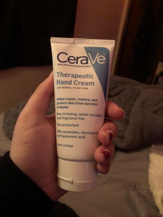 A hand is shown holding a tube of CeraVe Therapeutic Hand Cream, which is designed to repair, restore, and shield the skin from harmful irritants.