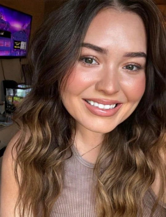 A reviewer with wavy hair smiling for a selfie, dressed in a casual sleeveless top