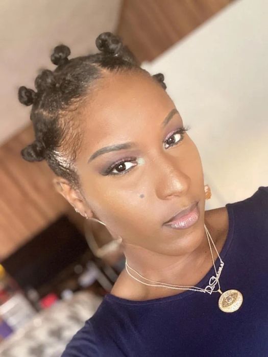 A reviewer sporting bantu knots, dressed in a dark top and a coin pendant necklace