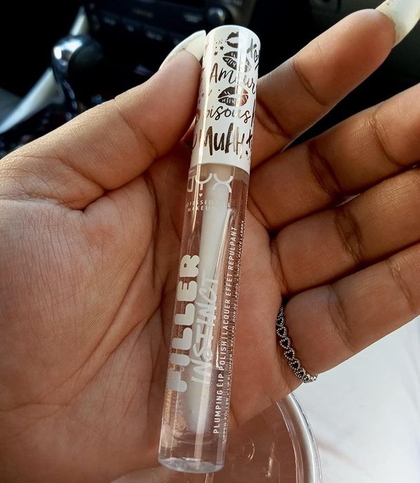 A reviewer holding a clear tube of lip plumping gloss.
