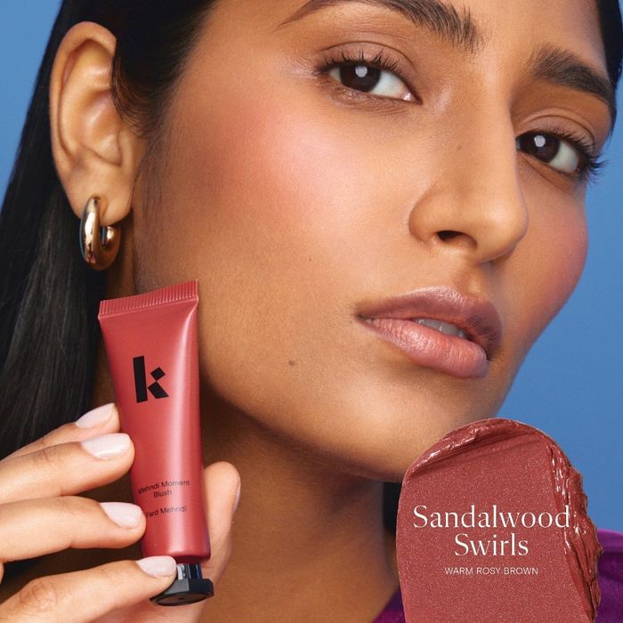 A woman holding a tube of K brand blush in the shade Sandalwood Swirls, accompanied by descriptive text.