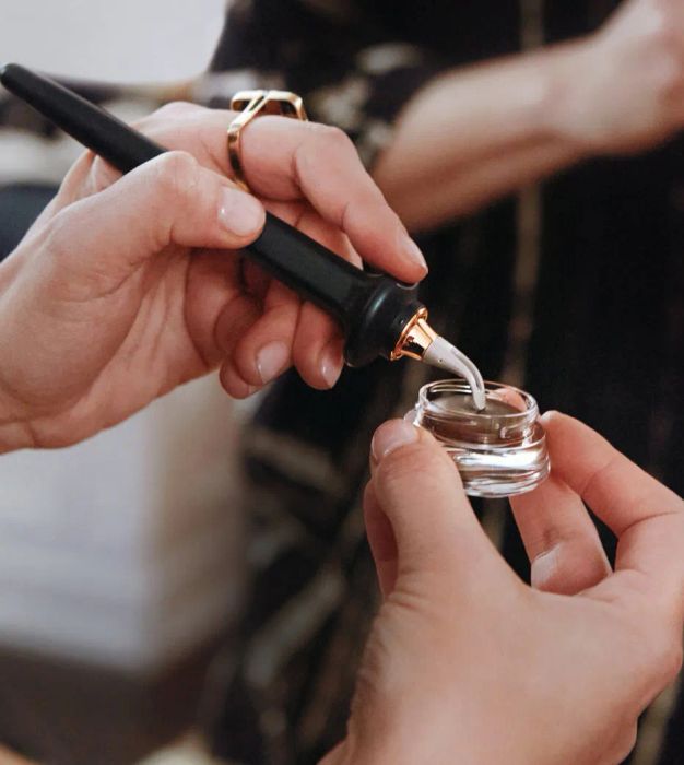 A model dipping the guide wand into a small pot of brown eyeliner.