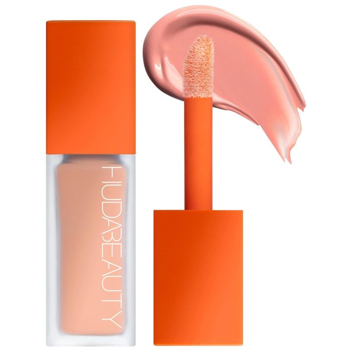 A Huda Beauty liquid lipstick in an orange tube, with the applicator displaying a glossy pink shade and the brand logo.