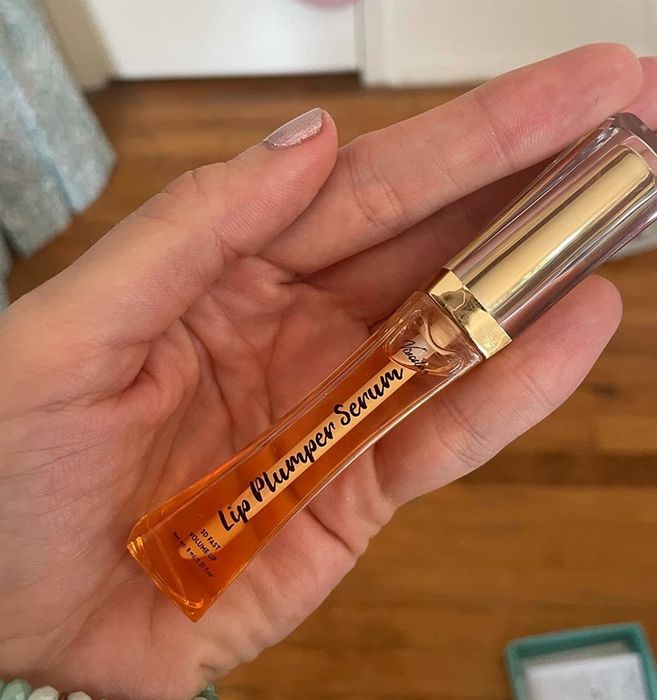 Reviewer holding a gold and orange-colored lip plumper tube.